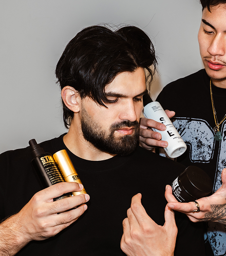 Two men holding and examining hair care products against a gray background

