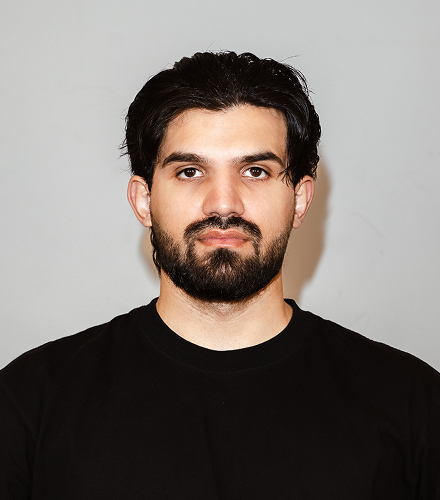 Man with a beard wearing a black shirt against a plain background

